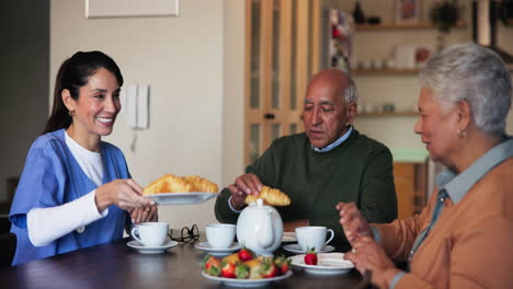 nurse serving tea and croissants to senior couple at home