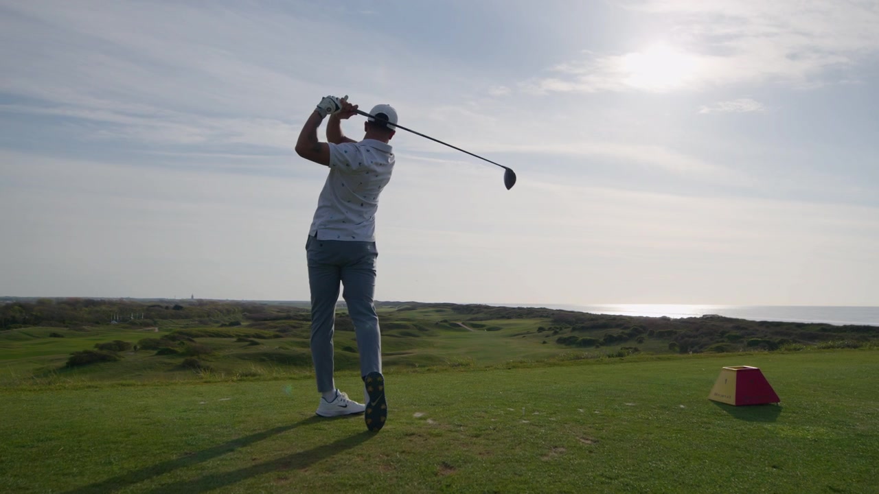 Golf driver shot swing of tee at seaside golf course, low angle slomo