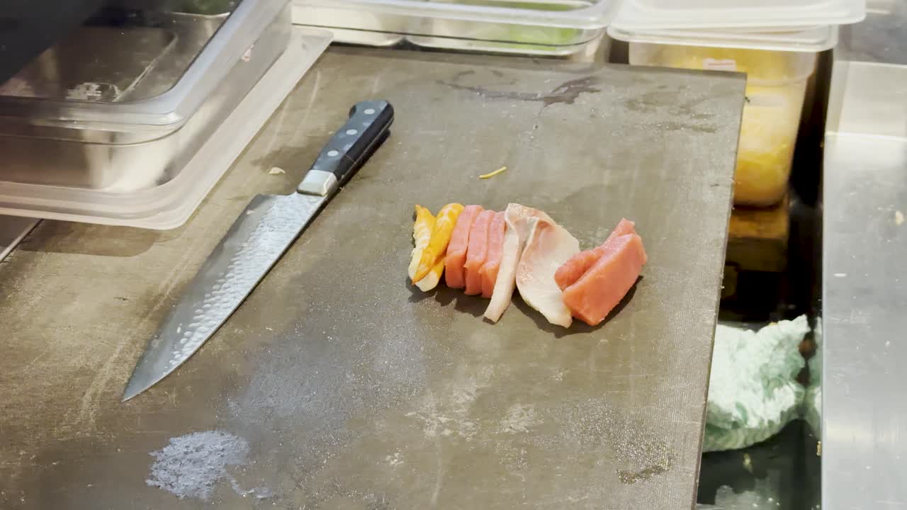 Vista dall'alto di uno chef che dispone un assortimento di sashimi accanto a un coltello sul bancone affollato di un ristorante