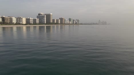 Misty-silver-sunrise-aerial:-Condos-and-calm-sea-at-Surfside,-Miami