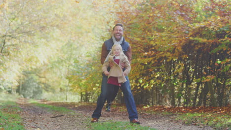 Father-Playing-Game-Picking-Up-Daughter-On-Family-Walk-Along-Track-In-Autumn-Countryside
