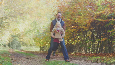 father playing game picking up daughter on family walk along track in autumn countryside
