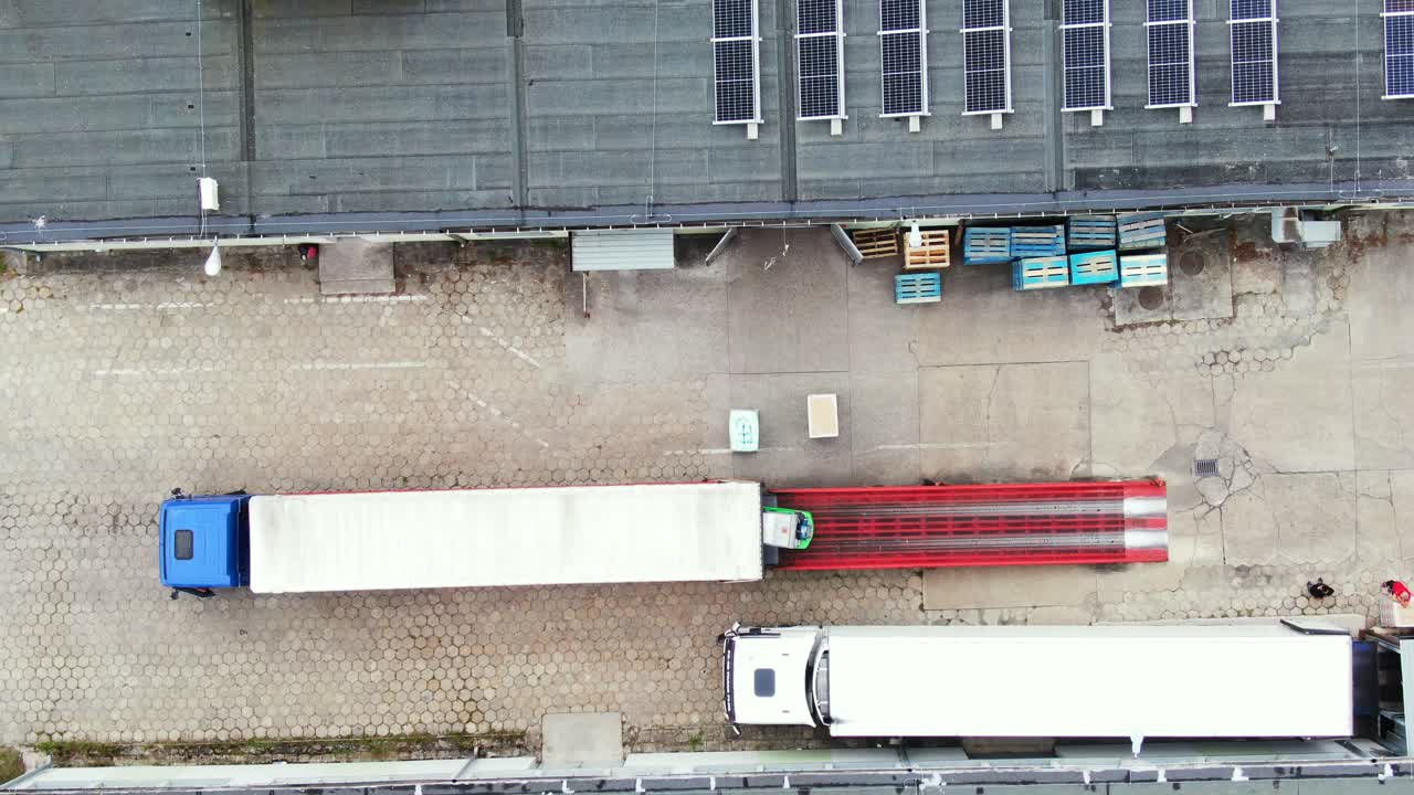Trucks with semi-trailers stand on the parking lot of the logistics park with loading hub and wait for load and unload goods at warehouse ramps at sunset