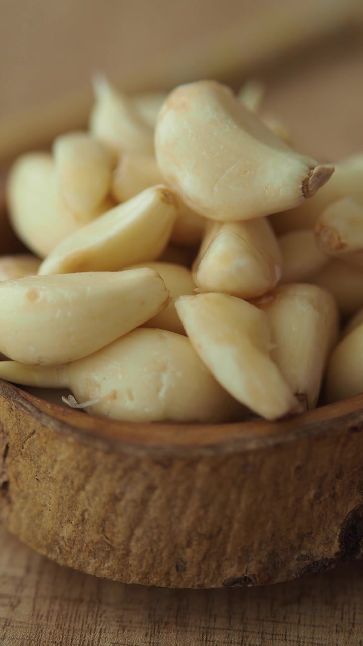 Primo piano di spicchi d'aglio freschi sbucciati in una ciotola di legno.