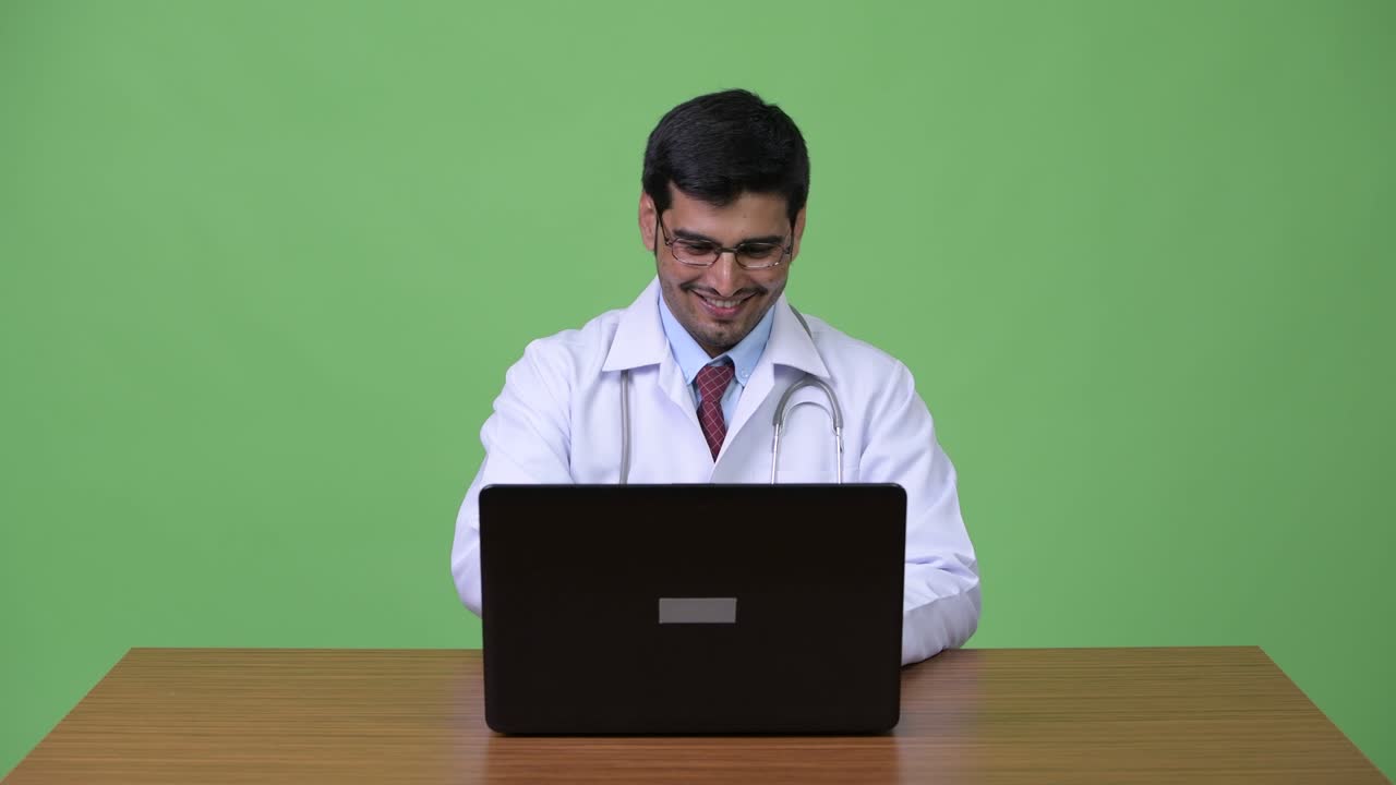 Young handsome Persian man doctor using laptop