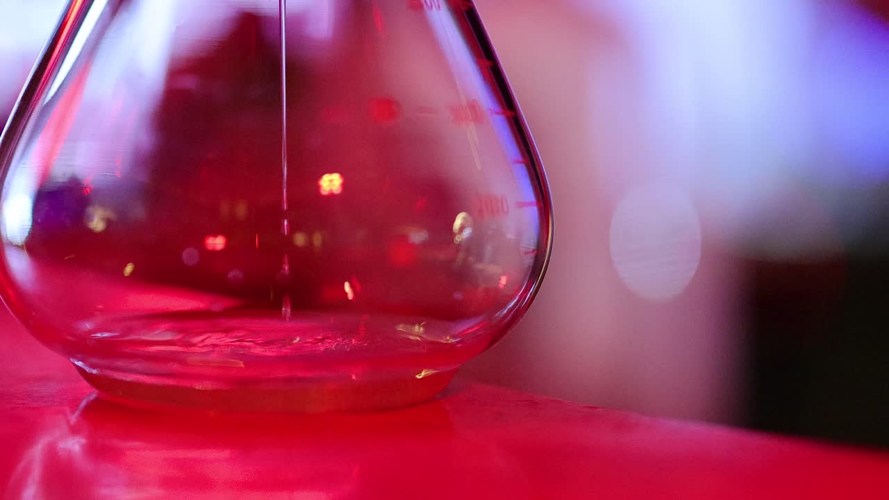 Macro shot of liquid drop entering cocktail glass, vibrant bar lighting, shallow depth of field