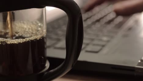 pouring fresh coffee into a pot with hands typing in background