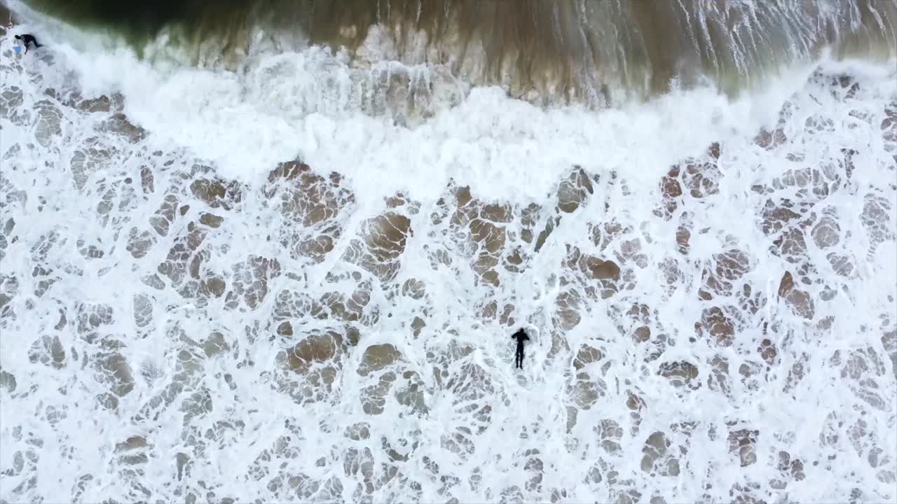 surfer paddling amongst the waves drone pov