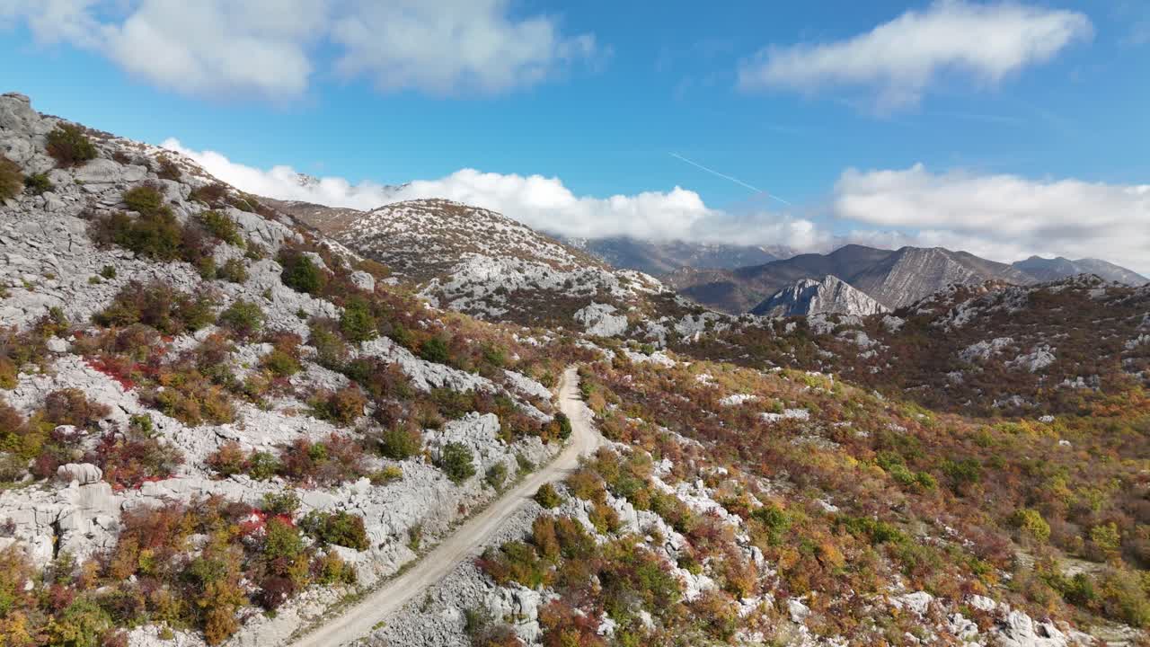Drone reveals successive autumn peaks of Velebit, glowing in orange hues with winding paths and the distant Adriatic, showcasing Croatia’s dramatic mountain wilderness in a sweeping aerial panorama