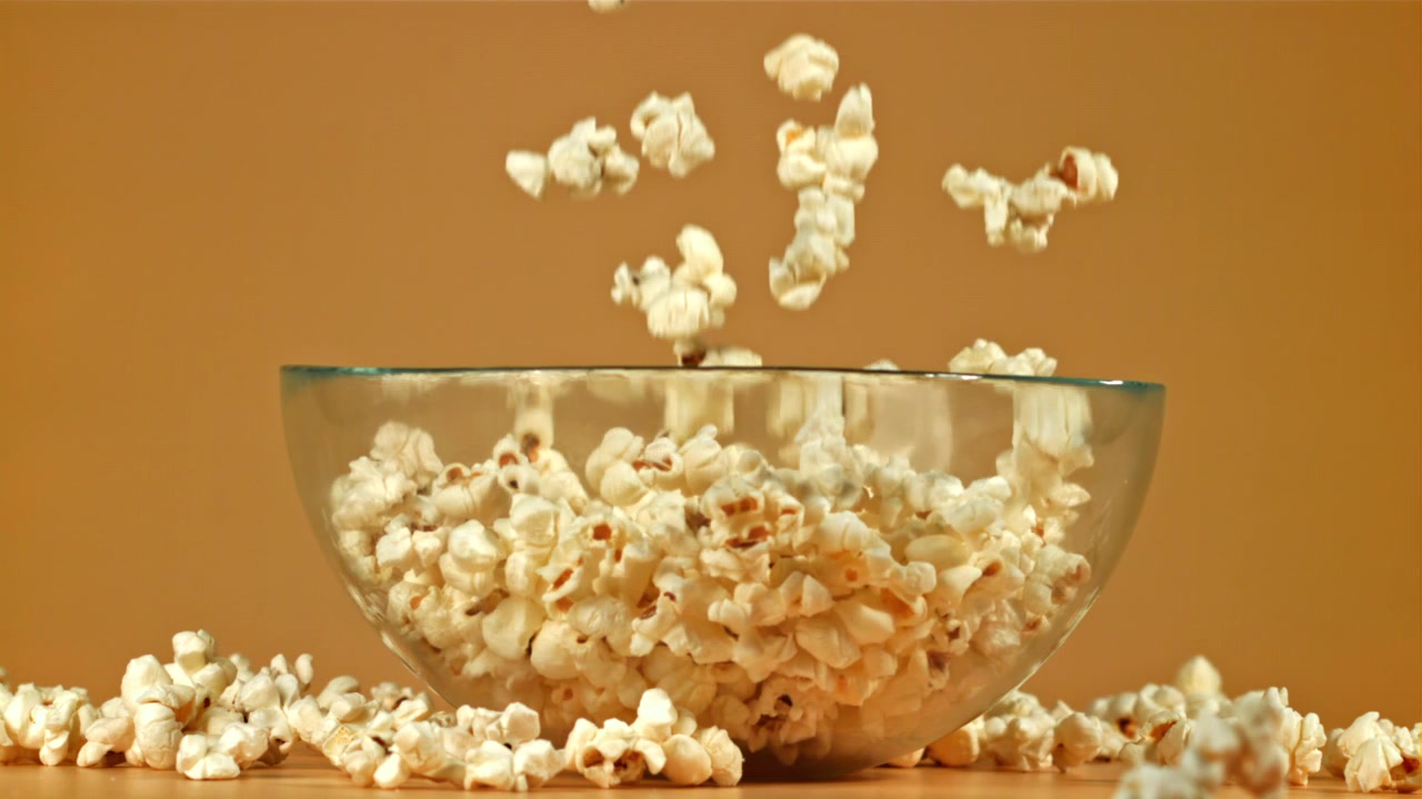 Popcorn freschi che cadono in una ciotola di vetro al rallentatore
