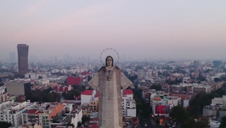 close up drone shots of massive jesus status towering over mexico city at sunset, featuring parroquia del purism corazon de maria and buildings in the back