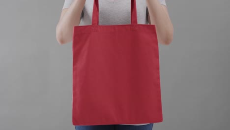 mujer caucásica con camiseta blanca sosteniendo una bolsa roja sobre un fondo gris, espacio de copia, cámara lenta