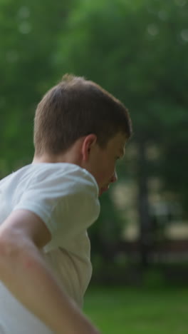 A young boy in a white shirt jumps while trying to maintain balance, with sunlight reflecting from above, the blurred background shows sports equipment and trees