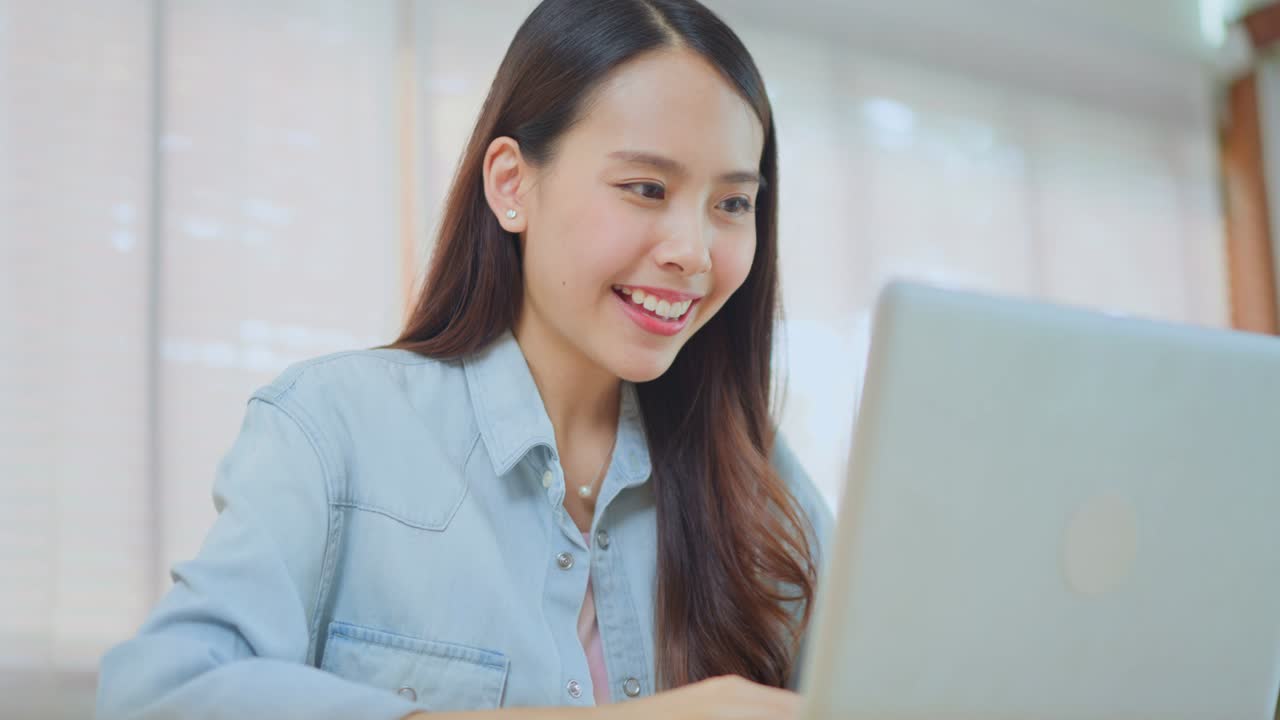 아시아의 매력적인 여자 학생은 집에 머물고, 집에서 거실에 앉아있다. 흥분 된 젊은 여성 우승자는 노트북을보고 좋은 소식을 알게 된 후 행복하게 느다.