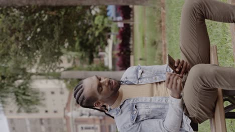 young man relaxing on a park bench while using his phone