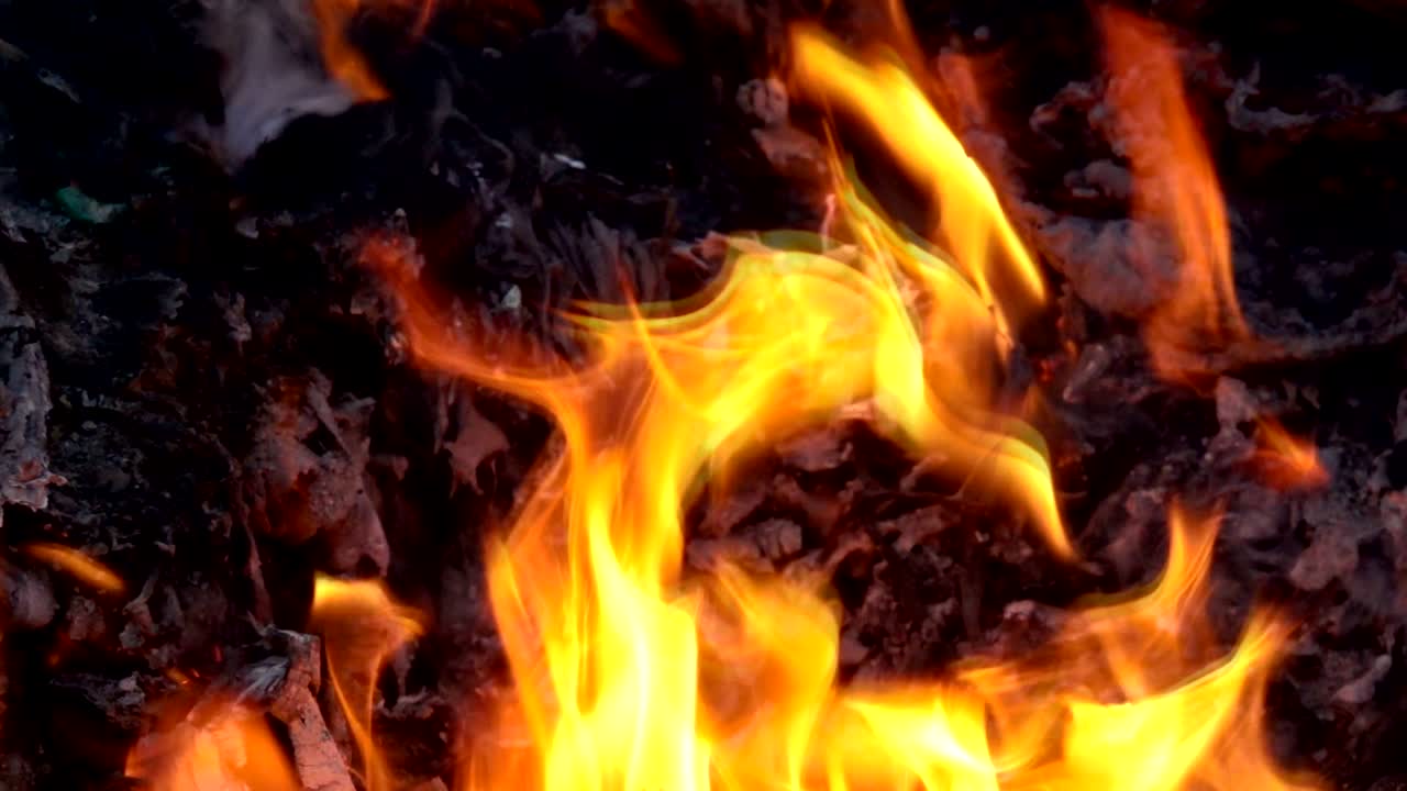 Fiamma e fumo a rallentatore che bruciano spazzatura o rifiuti su sfondo scuro.