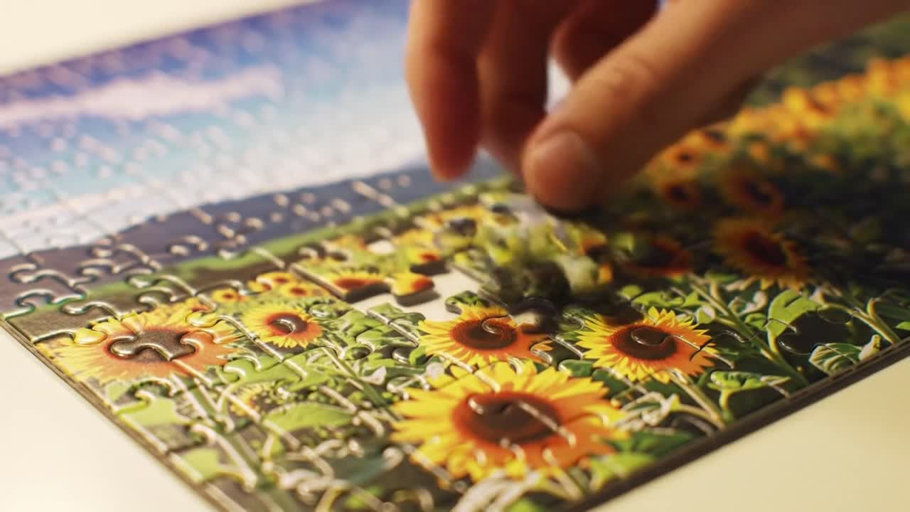 A hand carefully places the final pieces of a colorful sunflower puzzle during a tranquil evening, creating a sense of accomplishment and relaxation in a comfortable environment.