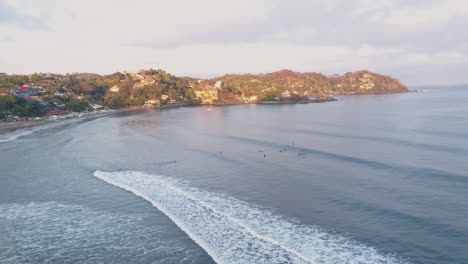 Orbiting-aerial-around-surfers-waiting-for-waves-in-water-by-coastal-town,-4K