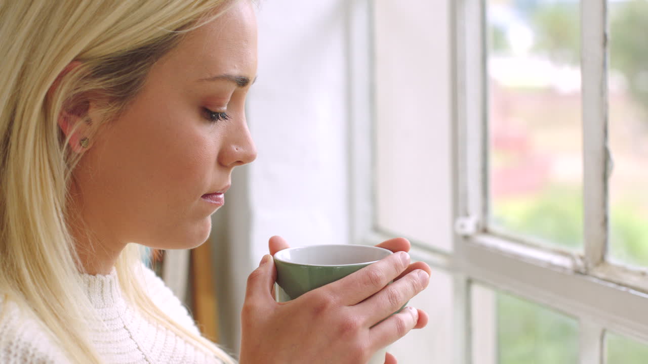 슬픈 여자가 밖을 바라보며 차를 마시고 있습니다.