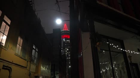 view of vancouver lookout tower glowing red in the distance from a view down a dark and dangerous alleyway side street littered with trash at night