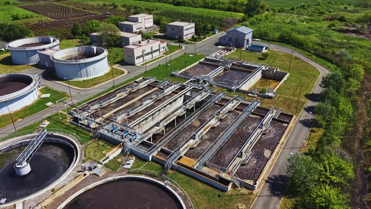 Industrial plant with clarifiers. Sunlit drone image of sewage processing complex. Capture of industrial sewage treatment site featuring tanks and vegetation from above