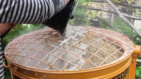 man putting lime into a hempcrete mixer with a bucket and gloves