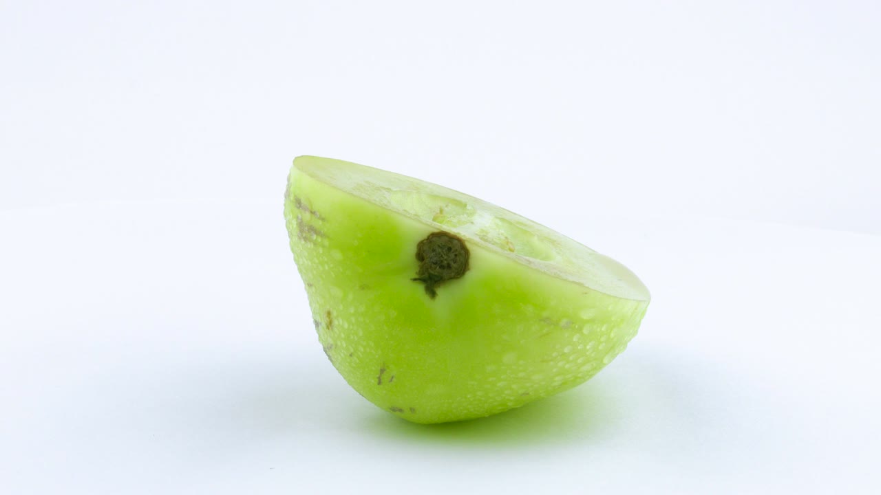 One half of green pepino with water drops. Rotating on the turntable. Isolated on the white background. Close up. Macro.