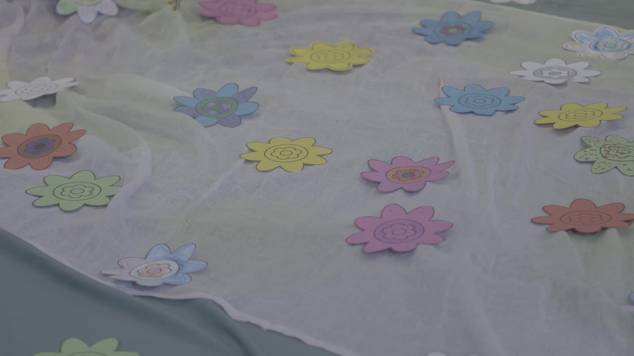 colourful, cut-out paper flowers lie on a white cloth on the floor