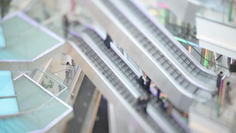 personas en movimiento en escaleras mecánicas en el centro comercial moderno. disparo con lente de cambio de inclinación con profundidad de campo súper superficial.