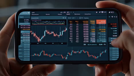 hands holding a smartphone displaying a financial trading app with charts