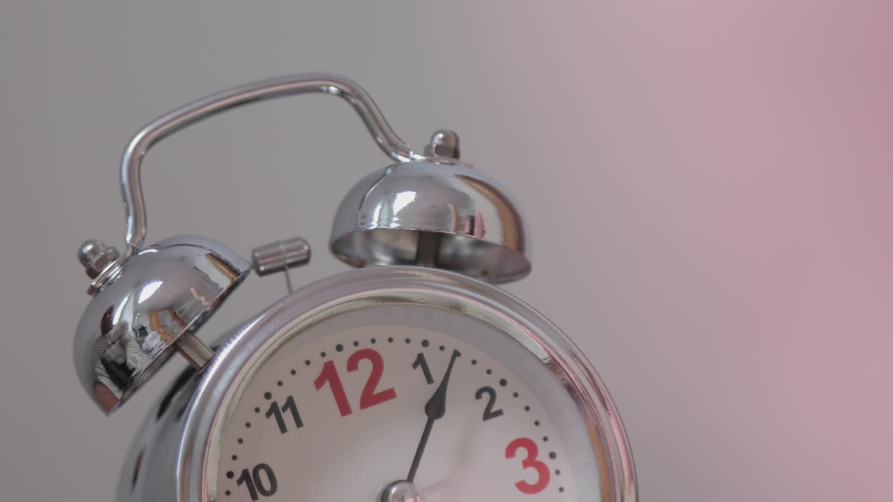 아침에 테이블 위에 있는 옛날의 알람 시계가 울리자, 소녀의 손은 알람을 뒤집어 닫고, 잠자는 소녀는 알람을 울리면서 깨어나서 알람을 꺼낸다.