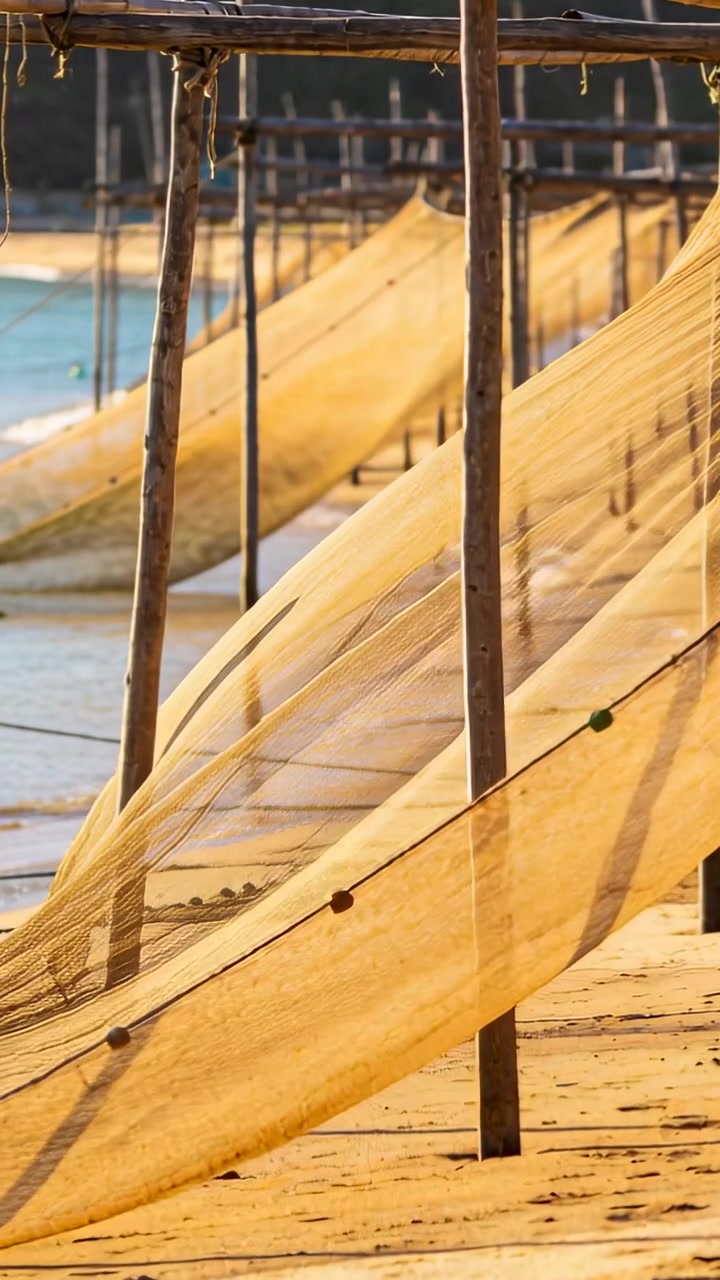 Vertikal video: Havbrise løfter gule fiskenet, der svajer langs en sandstrand med flåd.