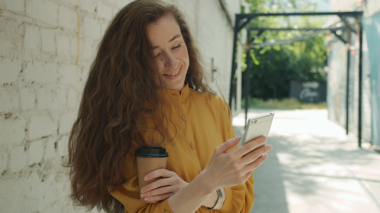 Woman using phone outdoors, holding coffee