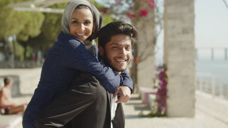 medium shot of arabic man carrying woman on back and smiling