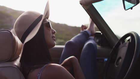 mujer afroamericana sentada con los pies en la ventana de un coche convertible