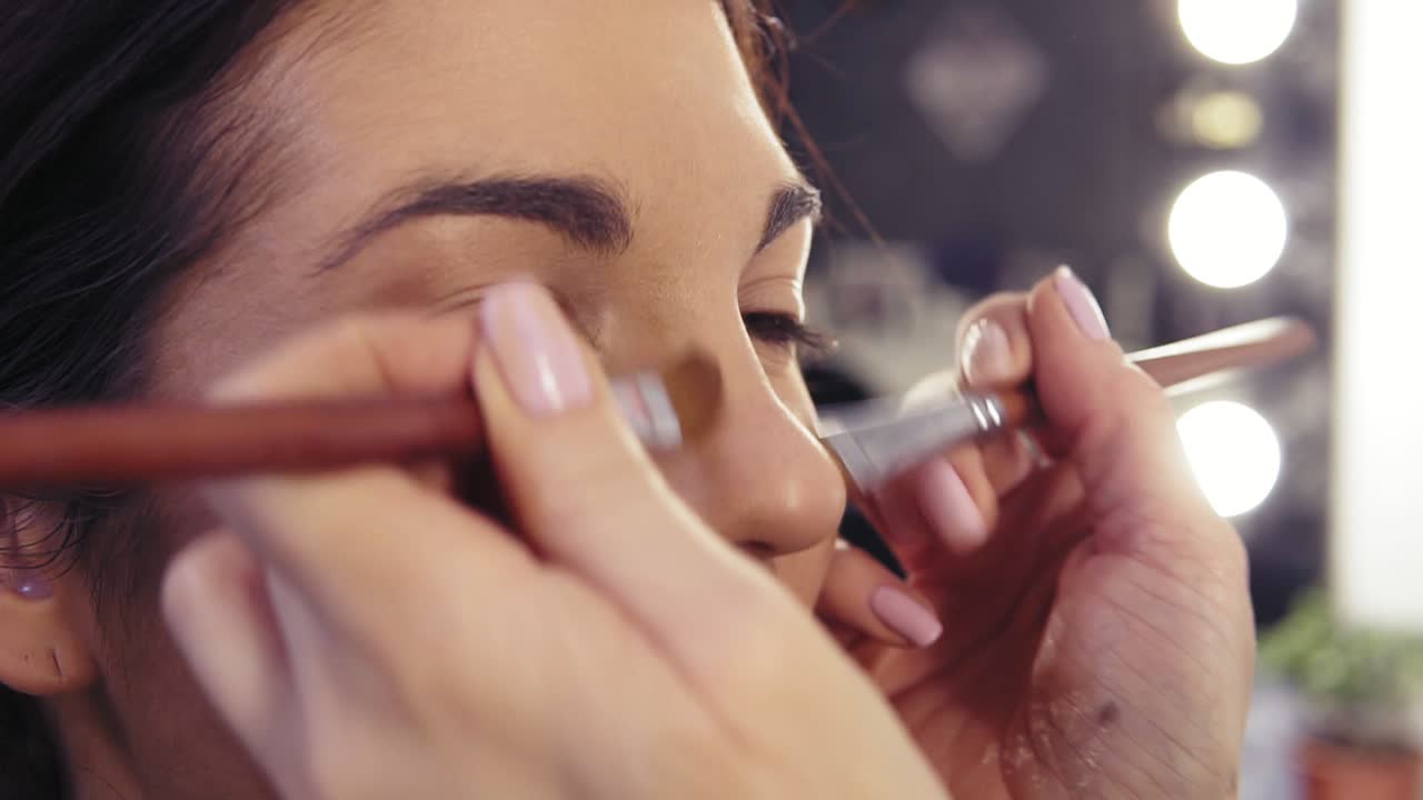 una joven morena hermosa con ojos de avellana esperando a un maquillador para terminar de contornear su nariz en un estudio de belleza.