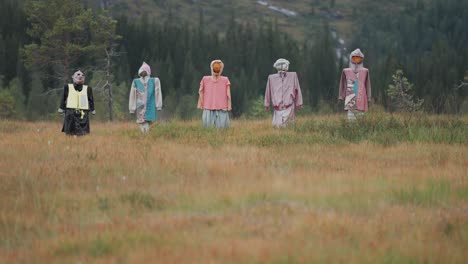 creepy scarecrows dressed in colorful clothing stand in the field