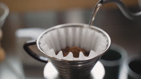 slow motion kettle pouring hot water over freshly ground coffee beans in filter paper