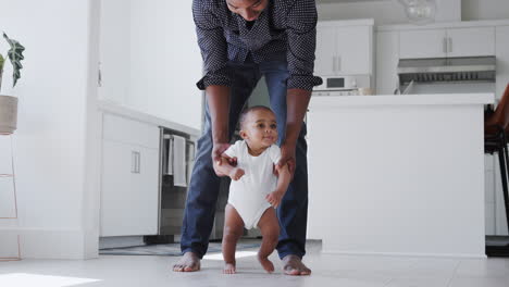 close up of father encouraging smiling baby son to take first steps and walk at home