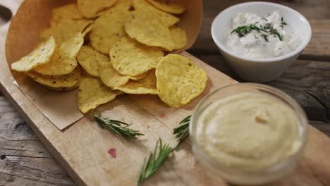 close up of potato chips and sauces on wooden tray on black surface