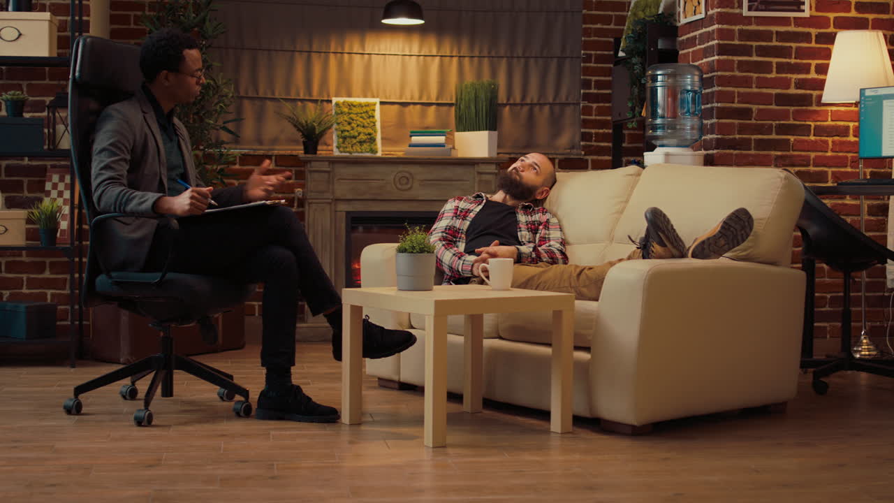 Psychologist attending therapy session with man laying on sofa