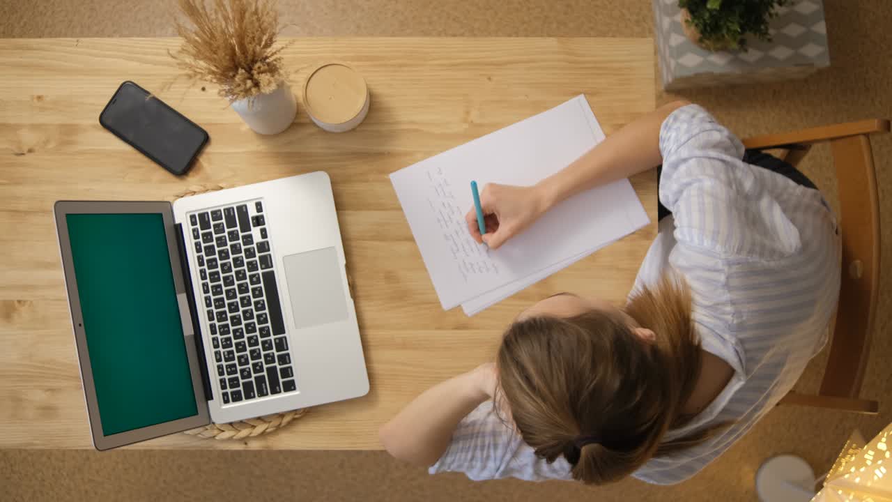 The girl writes down the main points from the conference. A laptop with a green screen. Top view. Remote work and training via the Internet. Make important notes on paper