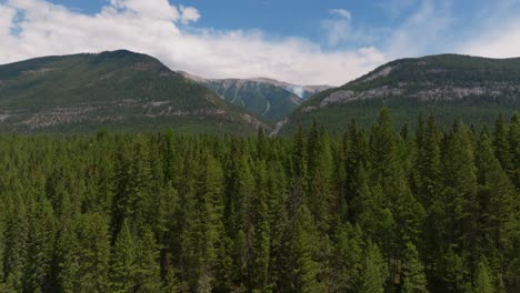 Drone-shot-rising-over-the-trees-to-show-mountains-in-the-distance-with-smoke-emanating-from-a-small-forest-fire-wildfire-in-British-Columbia-Canada-just-outside-Kootenay-National-Park