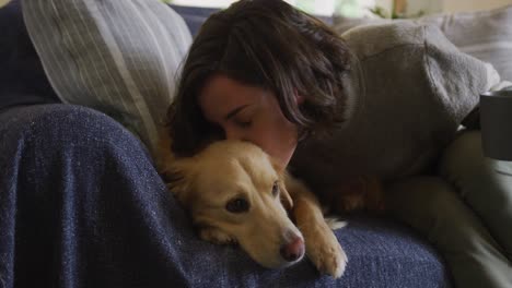 smiling caucasian woman kissing her pet dog sitting on sofa at home