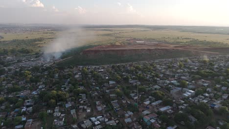 captivating 4k aerial footage features a dynamic push-in drone shot, seamlessly revealing a rural township village situated on the edge of a waste processing plant in south africa