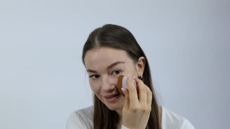 stunning young woman applying makeup on her face in the morning in front of a white background