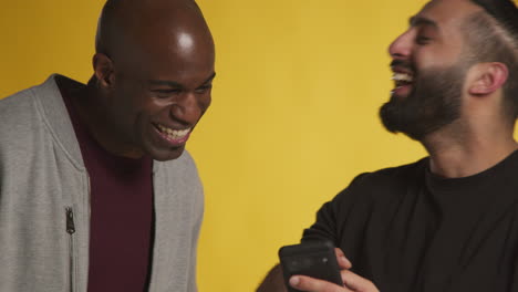 Fotografía-De-Estudio-De-Dos-Amigos-Varones-Emocionados-Con-Un-Teléfono-Móvil-Celebrando-Ganar-Dinero-Contra-Un-Fondo-Amarillo-1