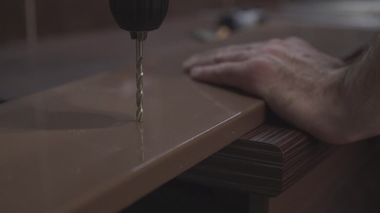 Furniture maker drills holes with a drill in the surface of the table Close-up
