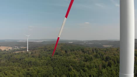 Aerial-boom-shot-slowly-decending-down-a-wind-turbine,-surrounded-by-countryside,-bright-blue-sky-day