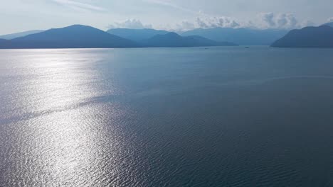 an aerial drone shot of the blue waters on the coast of lions bay under the morning sun with a single boat near the shore in front of a luxury property